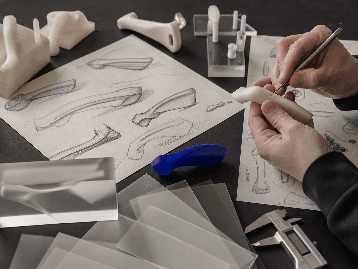 Hands working with sketches, study models, calipers, and translucent material samples